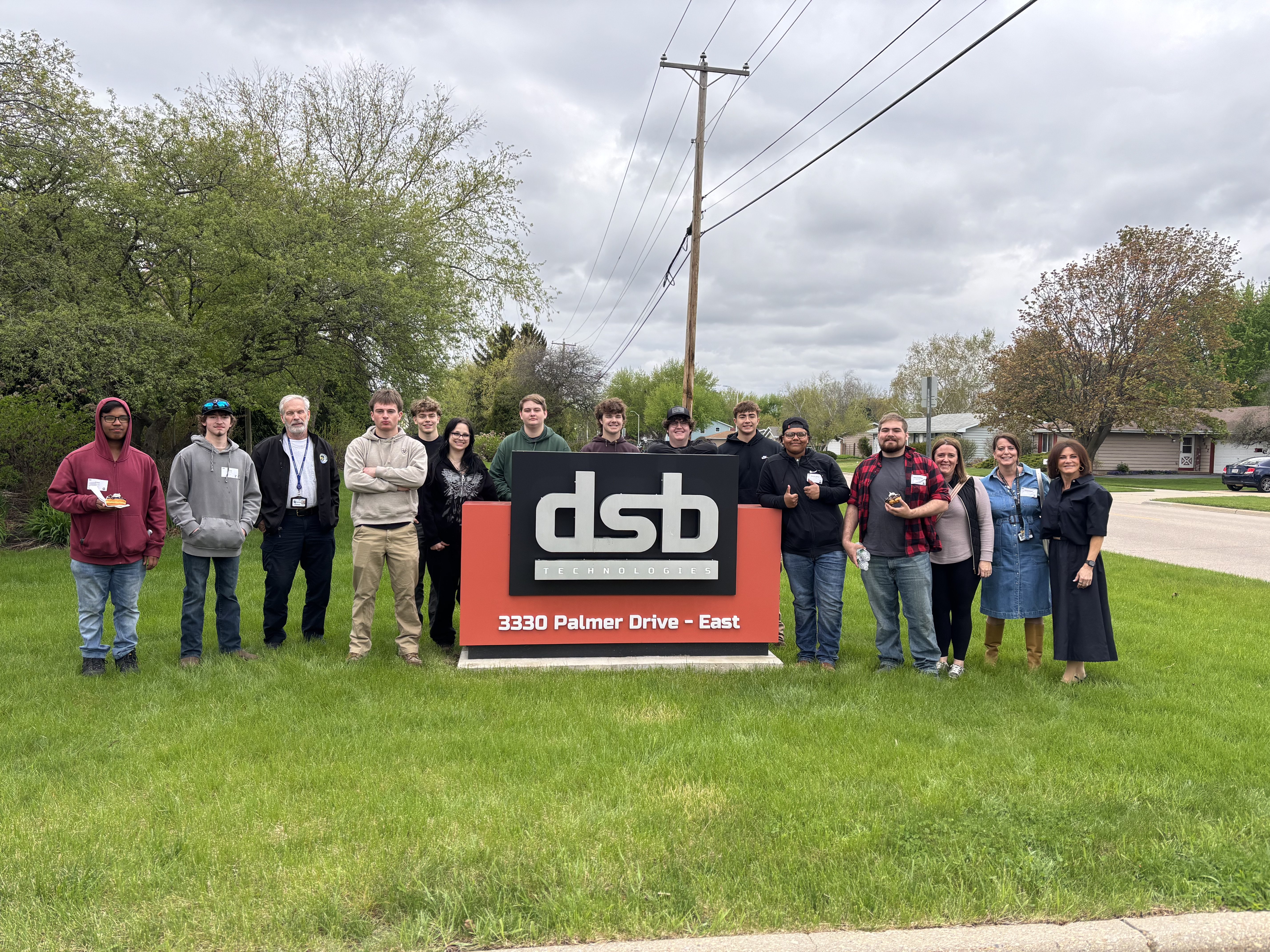 A group of students and staff posing outside next to the DSB Technologies company sign